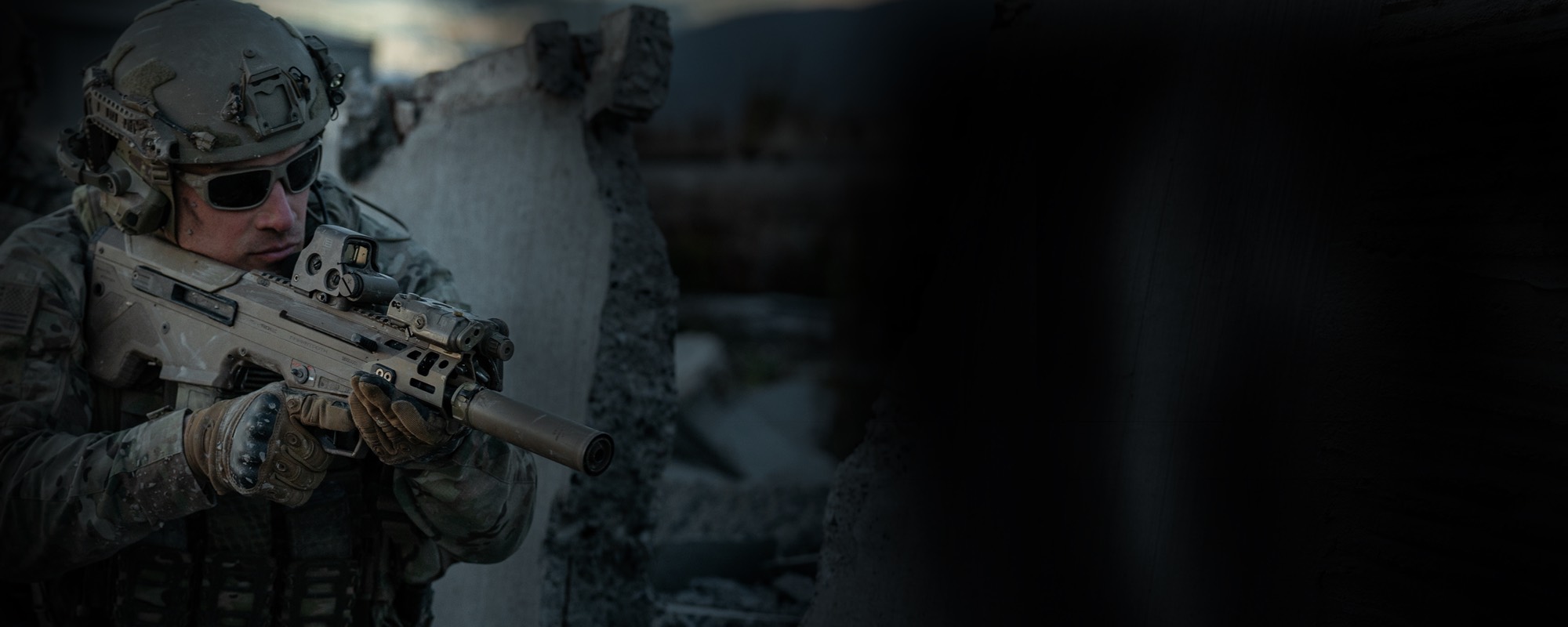 Operator aiming a suppressed WLVRN rifle around a concrete barrier